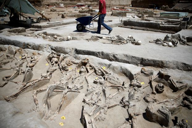 A worker pushes a cart next to shackled skeletal remains lying in a row at the ancient Falyron Delta cemetery in Athens